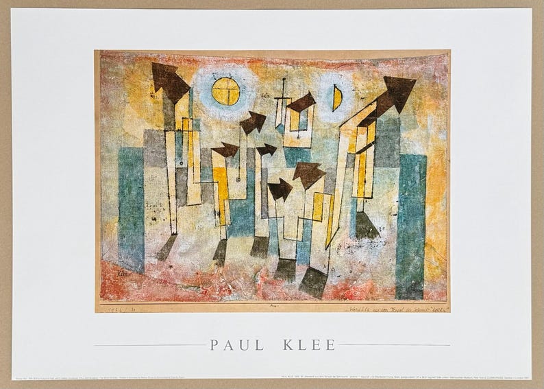 May include: A rectangular art print featuring a Paul Klee painting with abstract geometric shapes, arrows, and celestial forms in shades of yellow, blue, and brown. The name PAUL KLEE is printed in black capital letters centered below the artwork.