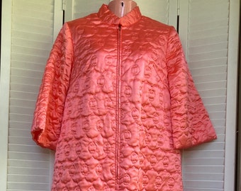 May include: A long, coral pink quilted robe with a zipper closure. The robe has a  pattern of small circles.