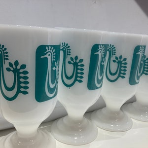 May include: Set of four white glass cups with teal blue stylized bird designs. The cups have a pedestal base.