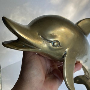 May include: A large, solid brass dolphin sculpture with a detailed, realistic design. The dolphin is depicted with its mouth open, as if it is about to leap out of the water.