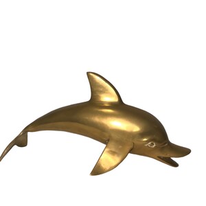 May include: A solid brass dolphin sculpture. The dolphin is leaping out of the water with its mouth open. The sculpture is a golden color.