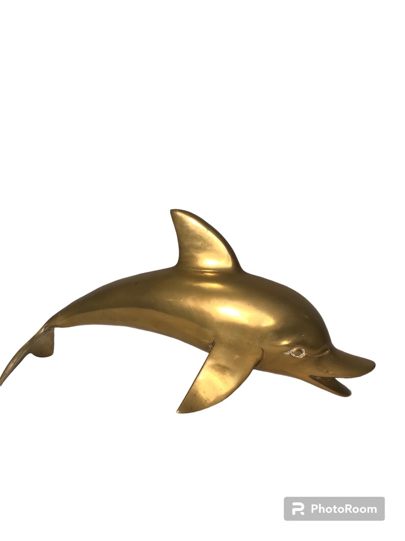 May include: A solid brass dolphin sculpture. The dolphin is leaping out of the water with its mouth open. The sculpture is a golden color.