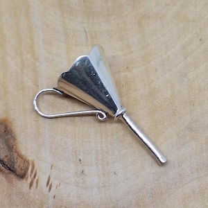 Puede incluir: Un pendiente plateado con un diseño único y estilizado. El pendiente presenta un elemento acampanado en forma de cono con un borde festoneado, conectado a un poste recto y un gancho curvo para la oreja. El pendiente está sobre una superficie de madera marrón claro.