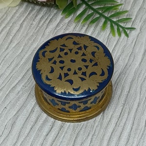 May include: A small, round, blue and gold trinket box with a decorative, intricate, gold design on the lid.