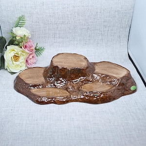 May include: A brown ceramic display stand shaped like a cluster of tree stumps with a glossy finish. The object features multiple flat, circular surfaces at varying heights, textured to resemble natural wood grain, and a small green sticker on the side.