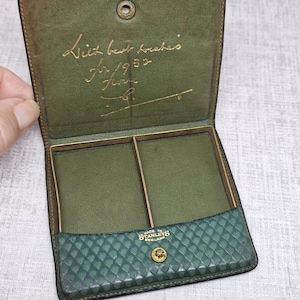 May include: Open green leather wallet with the inscription "With best wishes for 1952". The wallet has two compartments and a diamond-patterned lower section. The brand "Stanleys England" is visible.
