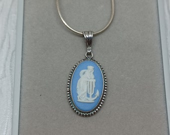 May include: Silver-toned necklace with a light blue oval pendant. The pendant features a white bas-relief design of a classical figure. The pendant is framed with a beaded border and hangs from a delicate silver chain.