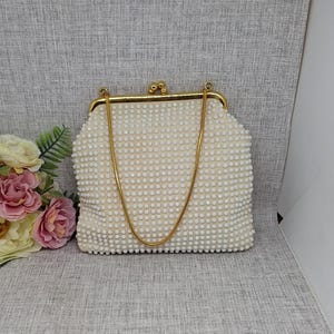 May include: Cream-coloured beaded handbag with a gold-tone metal frame and chain strap. The bag has a kiss-lock clasp and is decorated with small, round beads. The bag is a vintage style, possibly from the mid-20th century.