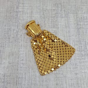 Op de afbeelding: Een vintage gouden mesh portemonnee met een cilindrische bovenkant en een driehoekig lichaam. De portemonnee is gemaakt van kleine, verbonden gouden schijfjes, waardoor een glinsterend effect ontstaat. De sluiting is ook goud.
