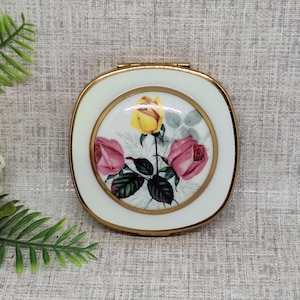 Poudre compacte vintage avec des roses roses et jaunes peintes sur un dôme en porcelaine entouré d'une bordure en émail blanc