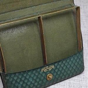 Pu&ograve; includere: Portafoglio vintage in pelle verde aperto, con dettagli dorati. L'interno presenta scomparti e un telaio in metallo. La parte inferiore ha un motivo a diamante. Il testo "MADE IN STANLEYS ENGLAND" &egrave; visibile.