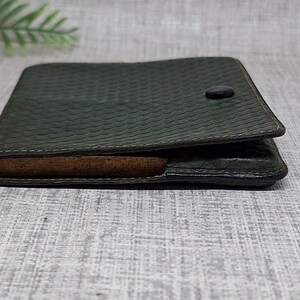 Pu&ograve; includere: Portafoglio in pelle verde scuro con motivo strutturato e chiusura con bottone. Il portafoglio &egrave; aperto, rivelando un interno marrone. Il design &egrave; semplice e classico, adatto all'uso quotidiano.