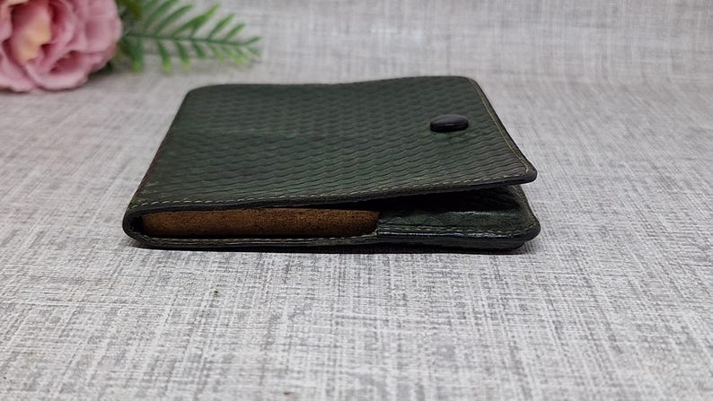 Pu&ograve; includere: Portafoglio in pelle verde scuro con motivo strutturato e chiusura con bottone. Il portafoglio &egrave; aperto, rivelando un interno marrone. Il design &egrave; semplice e classico, adatto all'uso quotidiano.