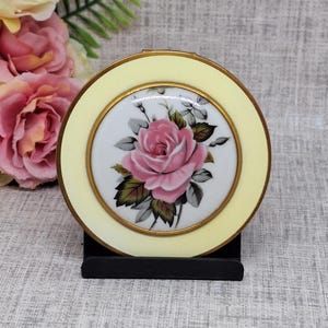 Poudre compacte vintage avec des roses roses peintes sur un dôme en porcelaine entouré d'une bordure en émail jaune