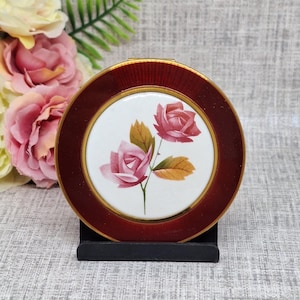 Poudre compacte vintage avec des roses roses peintes sur un dôme en porcelaine entouré d'une bordure en émail rouge