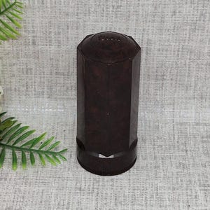 Puede incluir: Un tapón de botella octogonal de color marrón oscuro con una parte superior octogonal elevada. La parte superior tiene la palabra "París" en relieve.