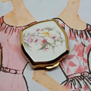 Mini boîte à pilules Stratton avec couvercle en émail blanc et décor de fleurs violettes et jaunes et de feuilles vertes dans des tons pastel roses