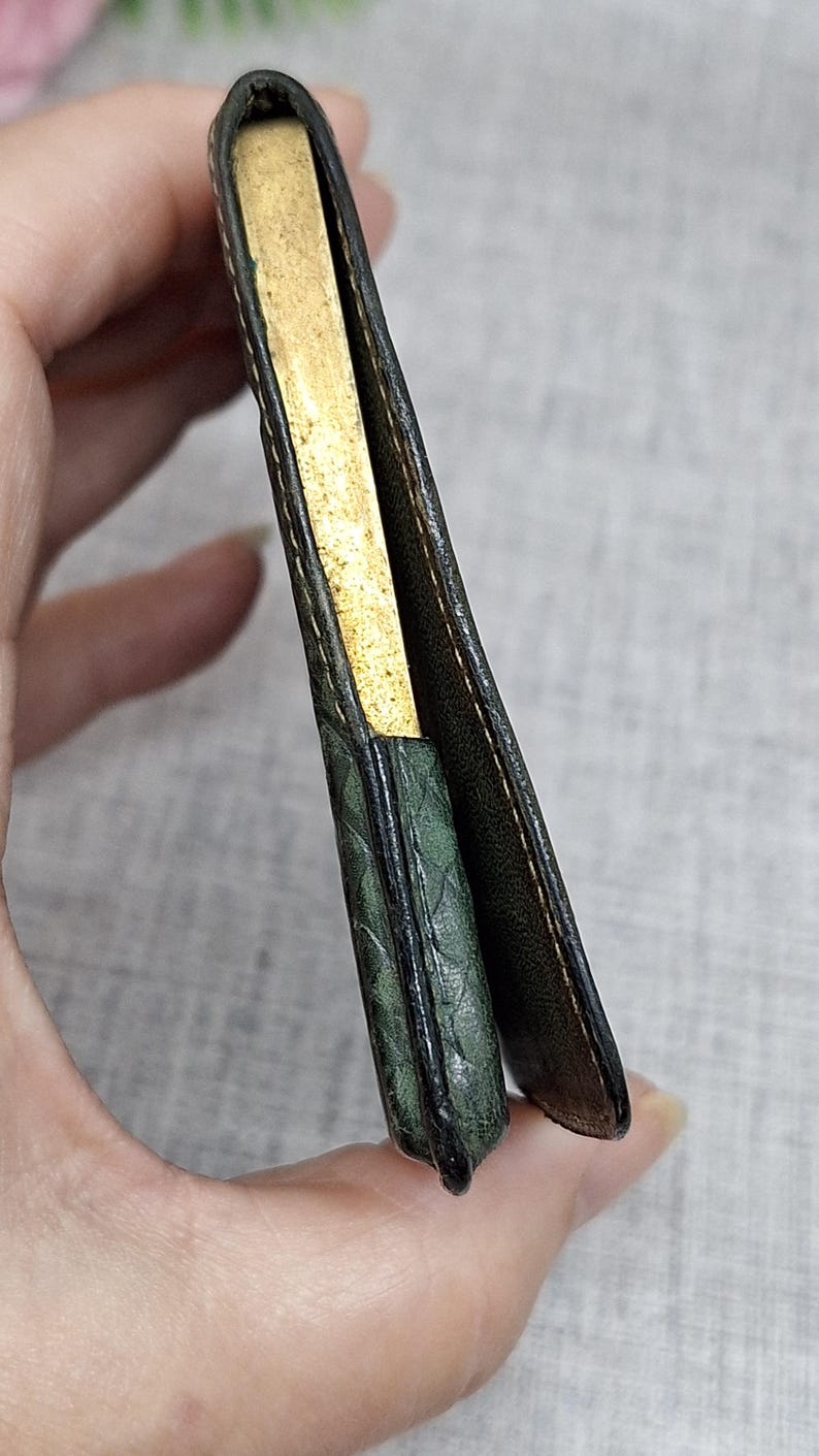 Pu&ograve; includere: Un portafoglio vintage aperto, che rivela un interno color oro. L'esterno &egrave; in pelle verde scuro con un motivo strutturato. Il portafoglio &egrave; tenuto aperto, mostrando l'interno e le cuciture dettagliate.