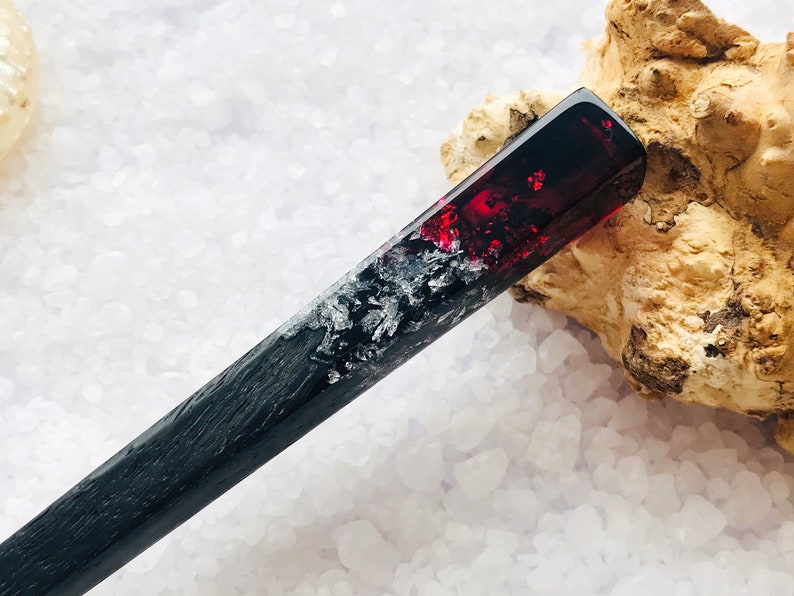 May include: A black and red hair stick with a red resin section containing silver glitter. The stick is resting on a white surface.