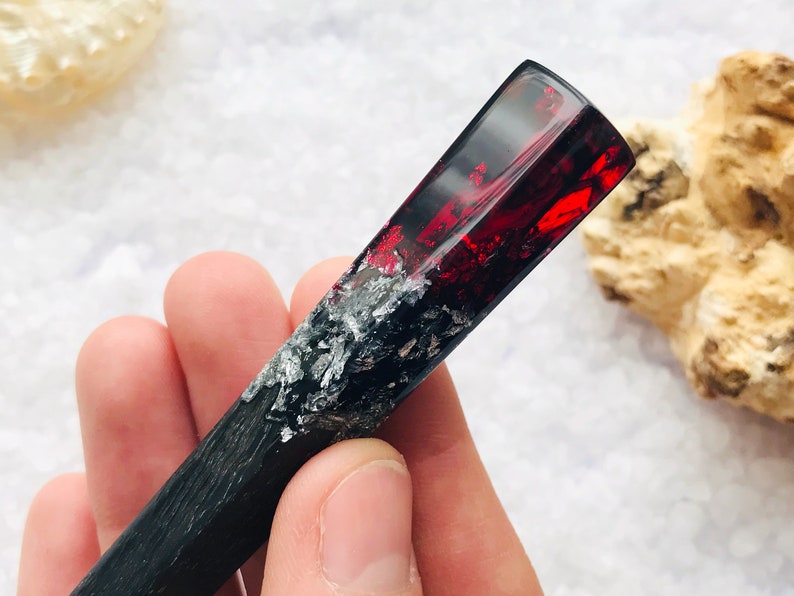 May include: A black and silver resin hair stick with a red and silver resin top. The stick is about 6 inches long.