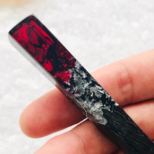 May include: A long, rectangular, black and red resin pendant with silver flecks. The pendant is made of two halves, one black and one red, with a clear line separating the two colors. The red half is translucent and has a swirling pattern.
