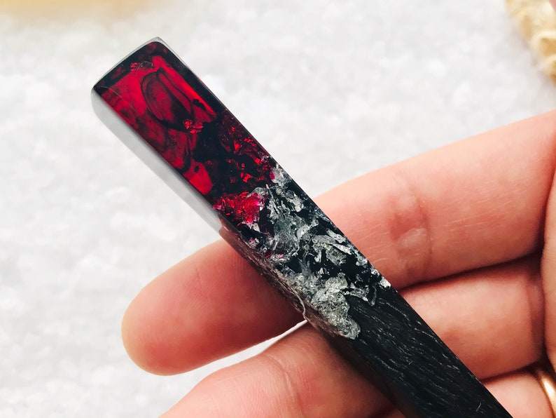May include: A long, rectangular, black and red resin pendant with silver flecks. The pendant is made of two halves, one black and one red, with a clear line separating the two colors. The red half is translucent and has a swirling pattern.