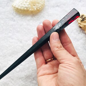 May include: Black and red resin hair stick with a sparkly finish. The stick is about 10 inches long and has a rounded end.