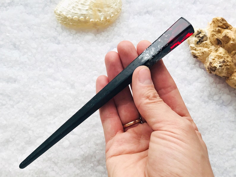 May include: Black and red resin hair stick with a sparkly finish. The stick is about 10 inches long and has a rounded end.