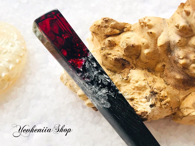 May include: A black and red resin hair stick with a swirling pattern. The stick is about 10 inches long and has a smooth, polished finish.