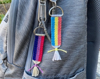 Puede incluir: Dos pulseras de amistad coloridas con borlas unidas a un tirador de cremallera plateado en una mochila gris.