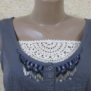 May include: A gray sleeveless top with a white crocheted lace trim and a beaded embellishment. The top has a button-up front.