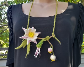 Può includere: Una collana di fiori di feltro con un fiore rosa e bianco, foglie verdi e perline verdi e bianche. La collana è su una camicia nera.
