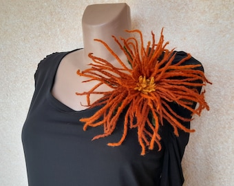Puede incluir: Una gran flor de fieltro naranja con un centro amarillo, prendida a una camisa negra.