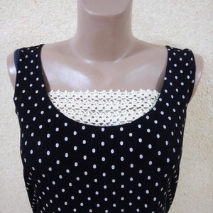 May include: Black sleeveless dress with white polka dots. The dress features a scoop neckline with a cream-colored crocheted lace insert. The dress is displayed on a mannequin.