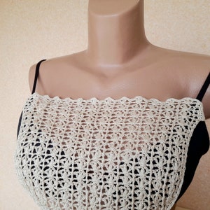 May include: A beige crochet top with a scalloped edge. The top is layered over a black tank top.