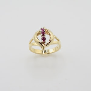 May include: A gold ring with a heart-shaped design and a row of red gemstones.