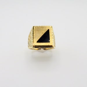 Könnte beinhalten: Ein goldener Ring mit einem schwarzen dreieckigen Stein, der in einen quadratischen Rahmen gefasst ist.