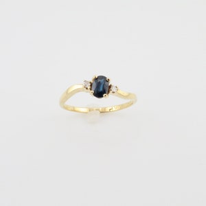 May include: A gold ring with a blue oval sapphire and two smaller diamonds. The ring is set on a white background.