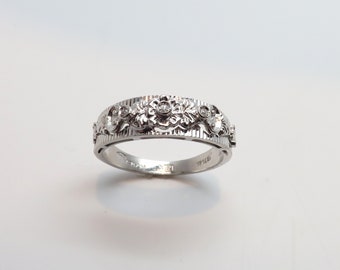 Op de afbeelding: Een zilveren bandring met een bloemmotief en kleine diamanten.