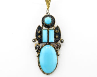 May include: A vintage pendant necklace featuring a large oval turquoise stone at the bottom, with two rectangular turquoise stones and a small round turquoise stone above. The pendant has a gold-tone metal frame with black accents and small clear crystals.