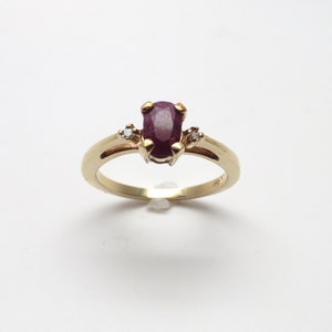 Può includere: Un anello d'oro con una pietra di rubino ovale rossa e due diamanti più piccoli.