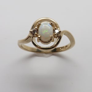 May include: A gold ring with an oval opal gemstone and two smaller diamond accents. The ring has a twisted band.