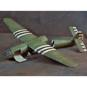May include: A scale model of a military transport glider painted in olive green with black and white invasion stripes on the wings and tail. The fuselage features an open cargo door and a cockpit with a grid-patterned window, accompanied by a small soldier figurine.