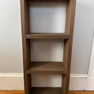 May include: A three-tiered wooden shelf unit with a dark brown stain. The shelf is made of solid wood and has a simple, rustic design.