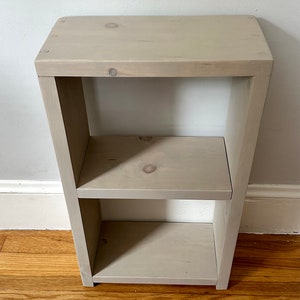 May include: A light gray wooden shelf unit with two shelves. The shelf unit is made of unfinished wood and has a simple, modern design.