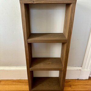 May include: A three-tiered wooden shelf unit with a dark brown stain. The shelf is made of solid wood and has a simple, modern design.