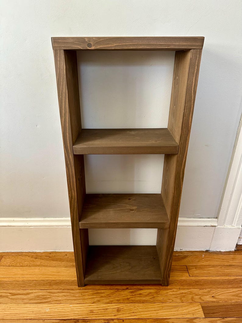 May include: A three-tiered wooden shelf unit with a dark brown stain. The shelf is made of solid wood and has a simple, modern design.
