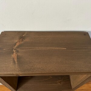 May include: A dark brown wooden shelf unit with a single shelf. The shelf is made of solid wood and has a natural wood grain.