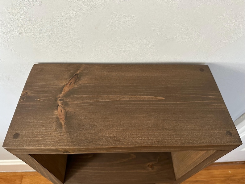 May include: A dark brown wooden shelf unit with a single shelf. The shelf is made of solid wood and has a natural wood grain.