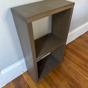 May include: A two-shelf wooden bookcase with a dark brown stain finish. The bookcase is made of solid wood and has a simple, modern design.